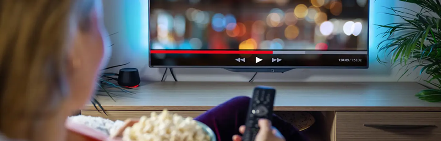 Kvinna äter popcorn och tittar på tv i hemmiljö