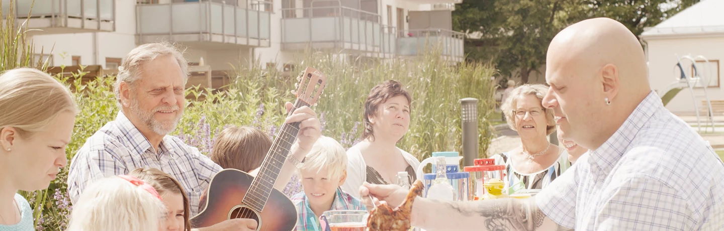 Hyresgäster som äter middag och spelar gitarr kring ett stort matbord utomhus