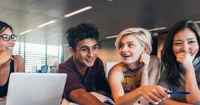 Tre personer sitter i gräset och studerar framför skärmar och block