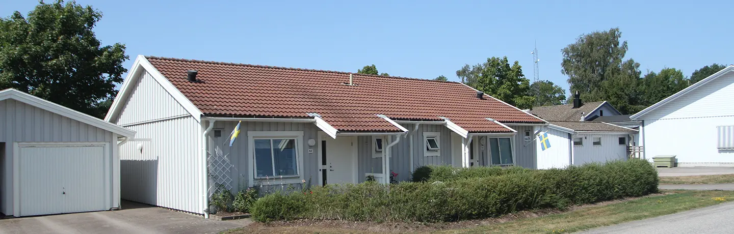 Enplans radhus i Åsaka med uteplats med omgivande häck och med ett garage vid sidan om.